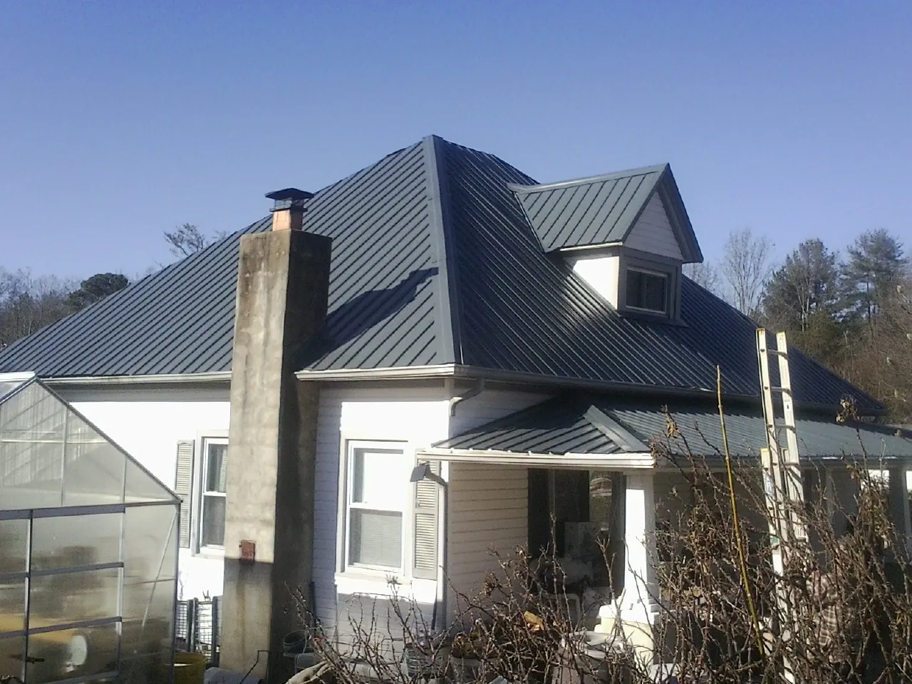 Dark blue standing seam metal roof on a white farmhouse with dormer — Slate & Tile Roof Repair by Roofing Brothers in Winterville