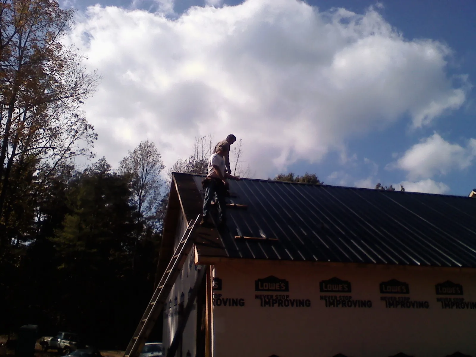 Roofer fastening dark metal panels high against a cloudy sky, from a Roof Inspection job in Winterville