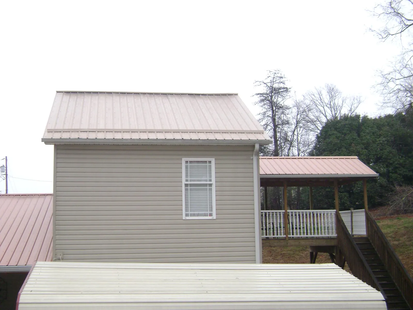 Tan metal roofs on a two story addition and attached porch, from a Roof Replacement job in Winterville