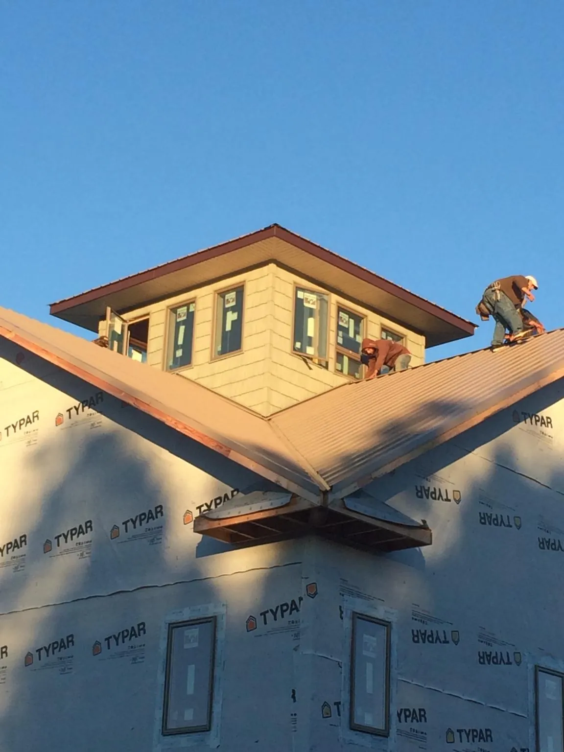 Roofers working around a rooftop cupola on a new metal roof at sunset — Roof Waterproofing in Winterville by Roofing Brothers